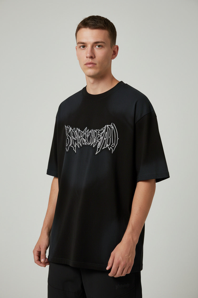 A black oversized short-sleeve t-shirt with a stylized white 'SPARKLE DEAD' graphic printed across the chest, displayed on a clean white background with text below.