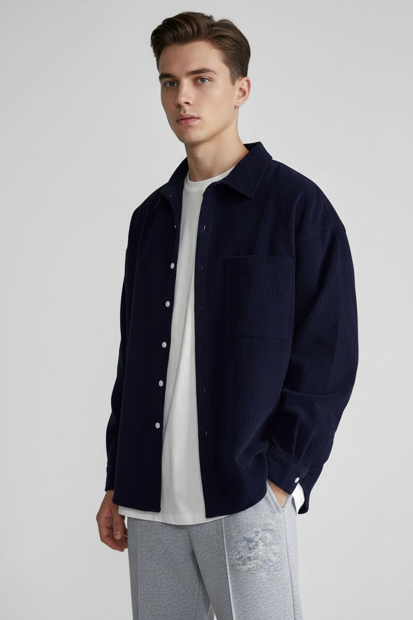 A person wearing an oversized dark navy corduroy button-up shirt over a white t-shirt and gray sweatpants, shown from the neck down against a plain white background.