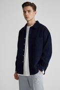 A person wearing an oversized dark navy corduroy button-up shirt over a white t-shirt and gray sweatpants, shown from the neck down against a plain white background.