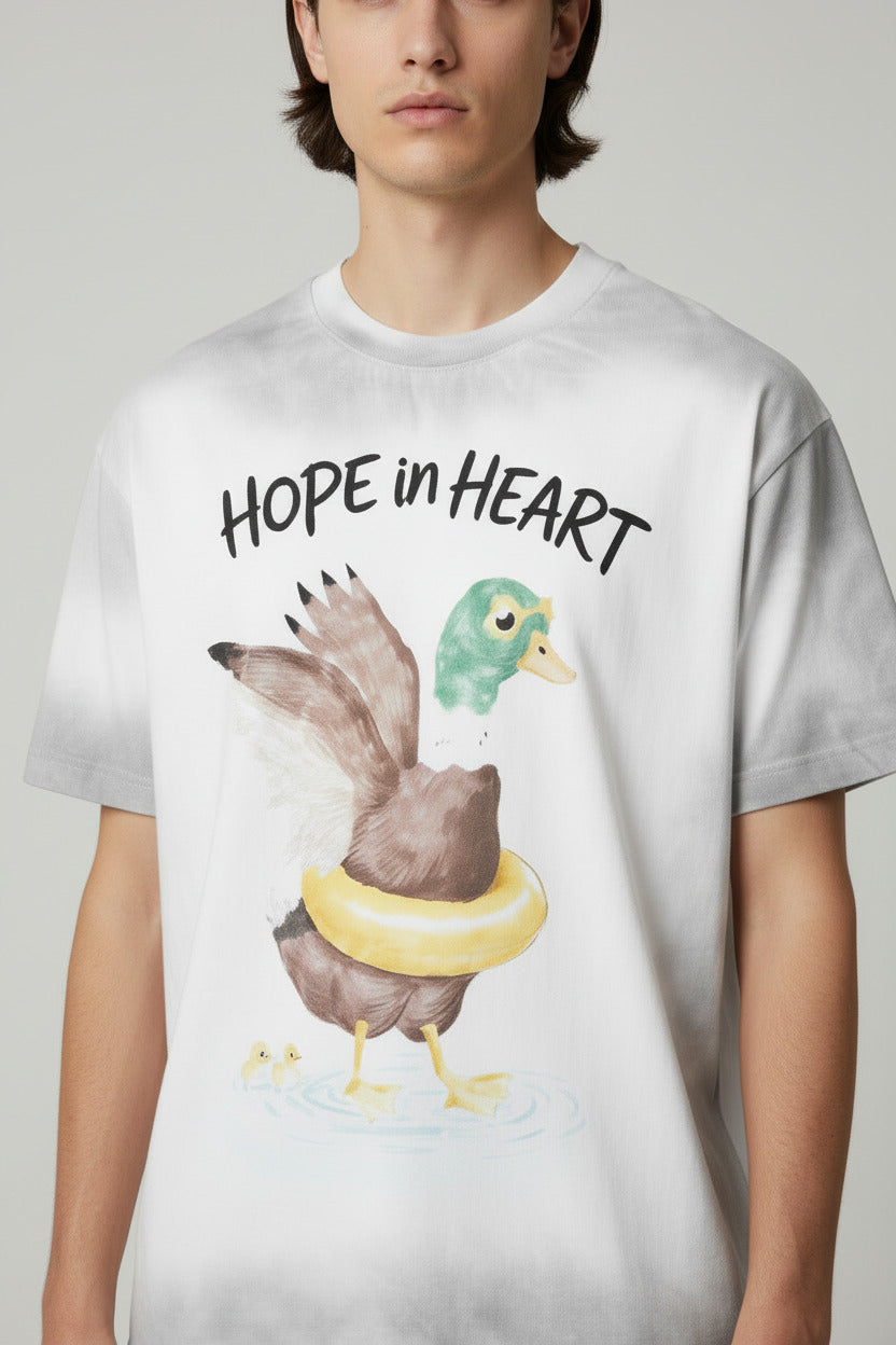 A white short-sleeve t-shirt with a gray tie-dye effect on the edges, featuring a watercolor graphic of a duck wearing a yellow life preserver with the text 'HOPE in HEART' above it. The t-shirt is displayed on a light gray background with a vertical brand label on the right side.