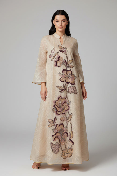 Woman in a floral embroidered dress standing in a sunlit archway with warm-toned walls.