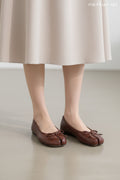 A pair of women's brown split-toe flats with bow details on the toes, held by a person sitting on a textured white rug.
