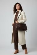 Brown woven handbag on a black surface with a white wall background