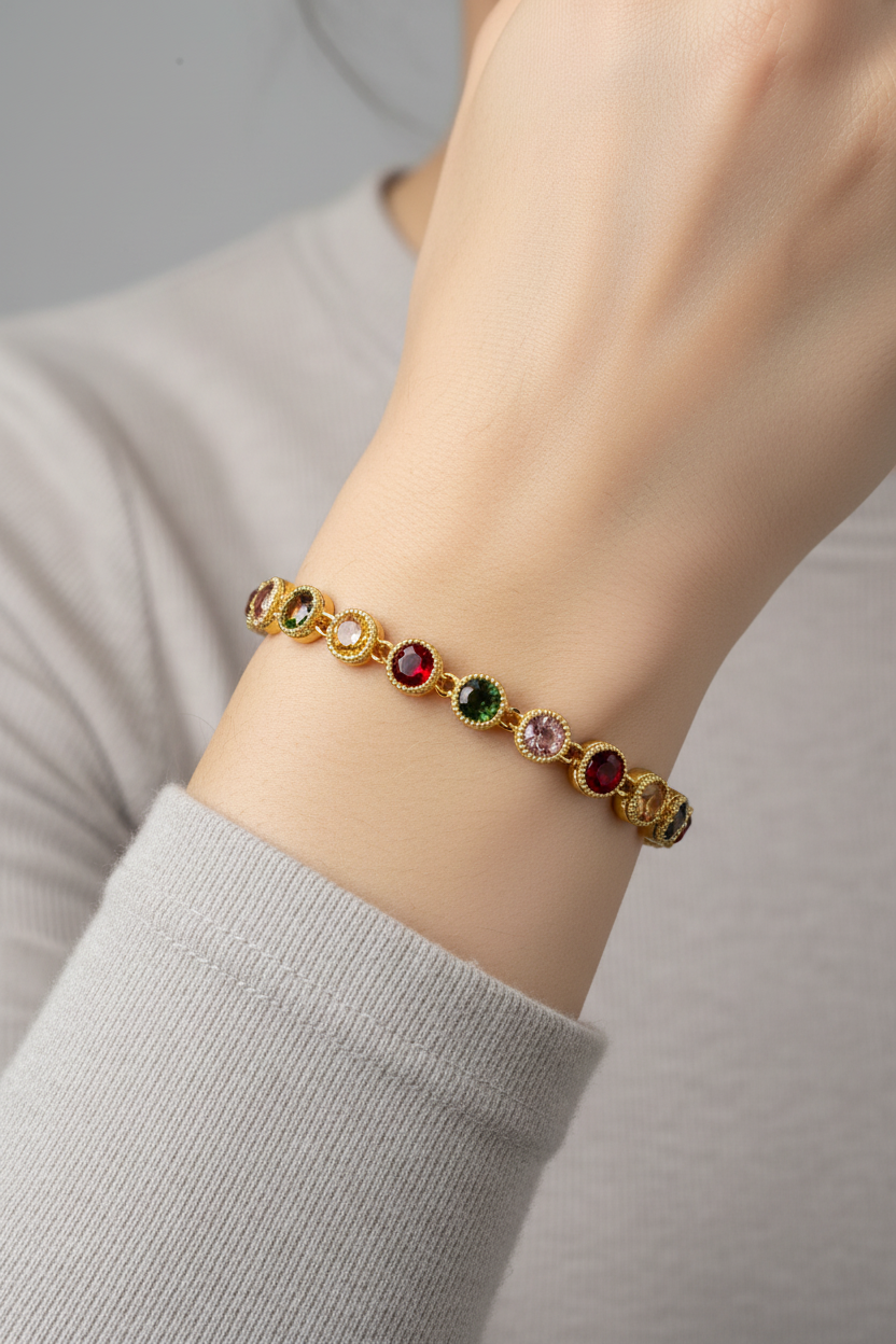 A gold-plated bracelet with oval multicolor gemstones, shown worn on a person's wrist. The bracelet features alternating oval links in red, green, pink, yellow, and light purple, set in a textured gold-tone metal.