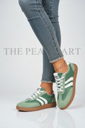 A pair of green and white low-top sneakers with a gum sole, shown on a model wearing blue jeans against a white background.