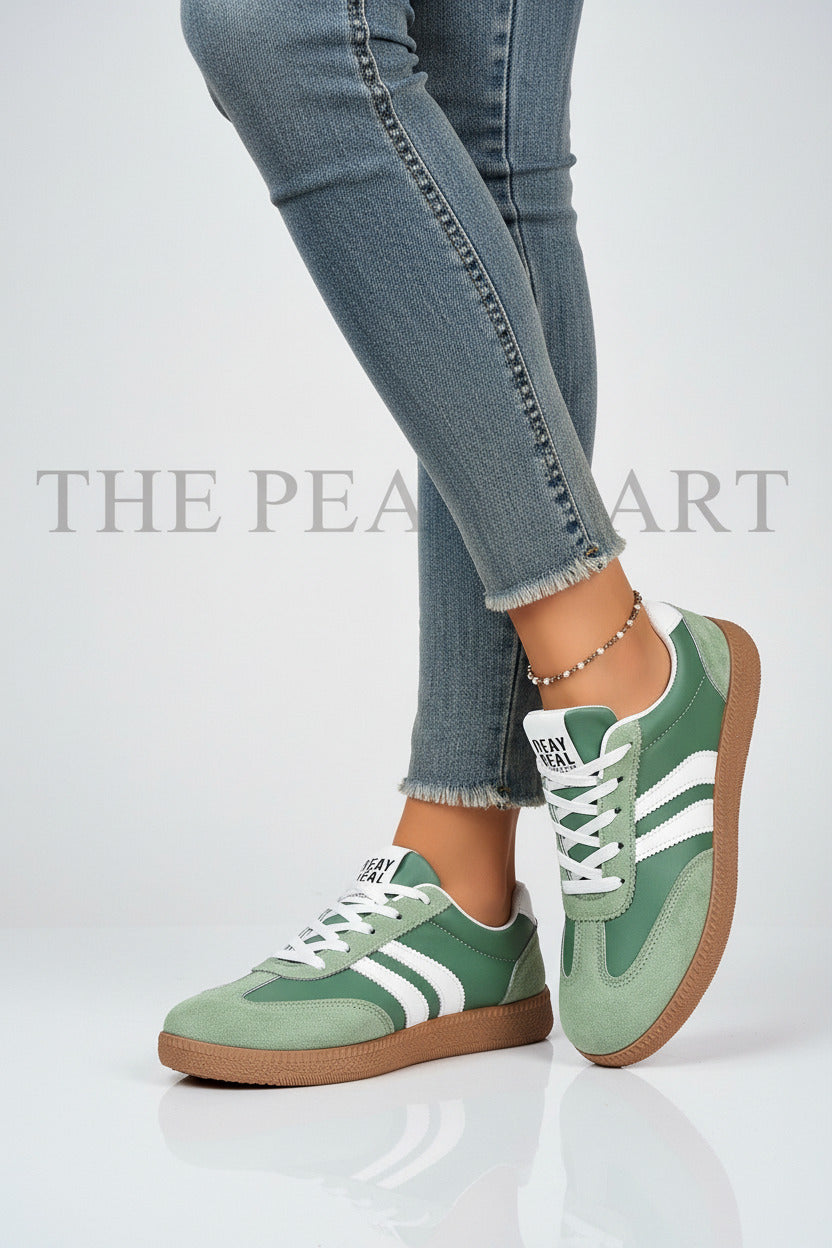 A pair of green and white low-top sneakers with a gum sole, shown on a model wearing blue jeans against a white background.