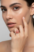A rose gold ring featuring a cherry blossom flower with red enamel petals and a clear central gemstone, shown on a soft pink background with a small '360-degree free rotation' text overlay.