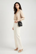 A black quilted leather drawstring bucket bag with gold-tone chain straps and bead accents, worn crossbody by a model wearing a beige blazer.
