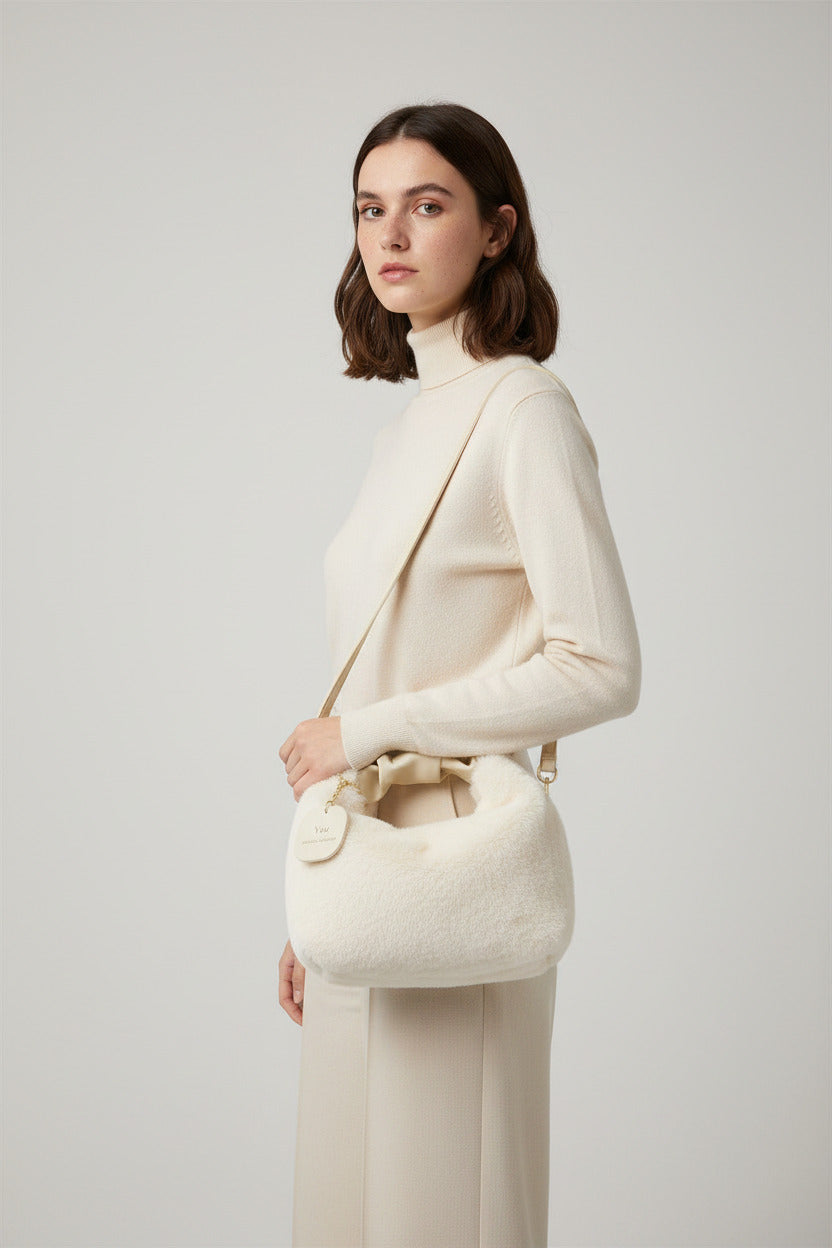 White fluffy handbag with gold chain handle held by a person, with blinds and text in the background.