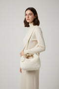White fluffy handbag with gold chain handle held by a person, with blinds and text in the background.