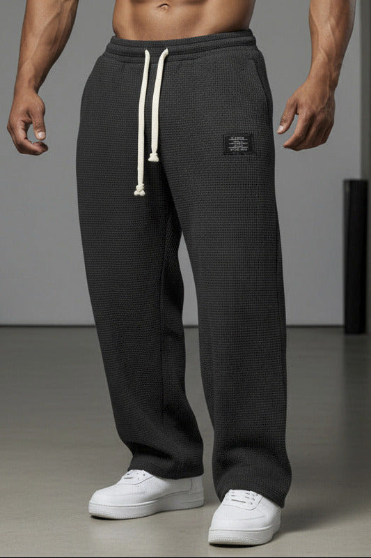 Person wearing black textured sweatpants with a white label on a white background
