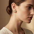 Gold earrings with diamond accents on a beige fabric background