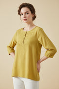 Yellow embroidered blouse on a hanger with a wooden table and plant in the background