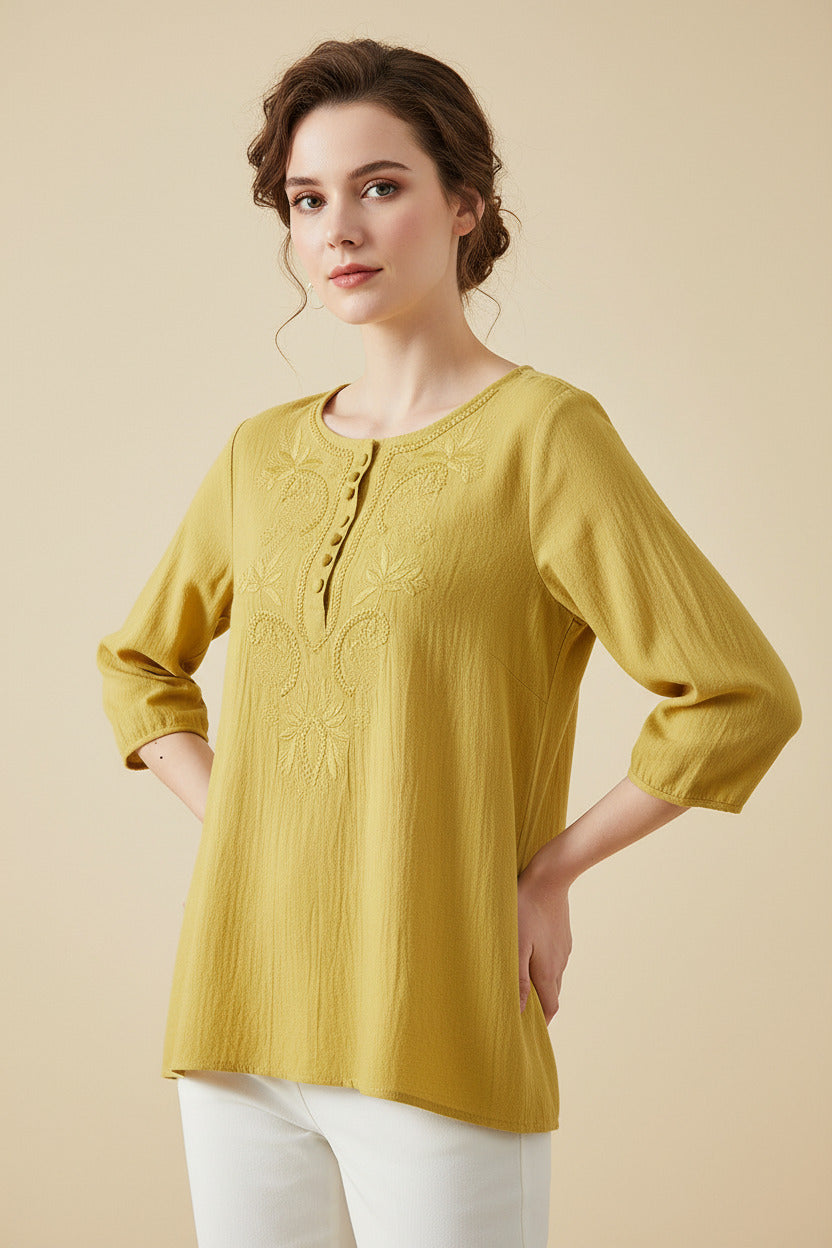 Yellow embroidered blouse on a hanger with a wooden table and plant in the background