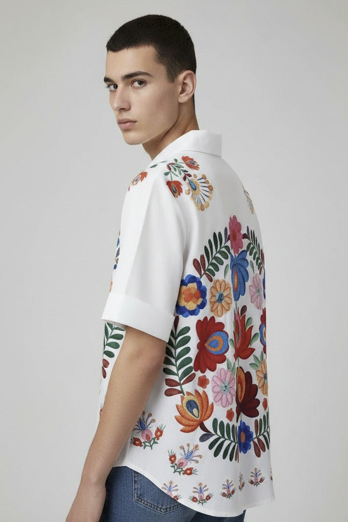 White shirt with colorful floral embroidery on a hanger against a neutral background