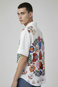 White shirt with colorful floral embroidery on a hanger against a neutral background