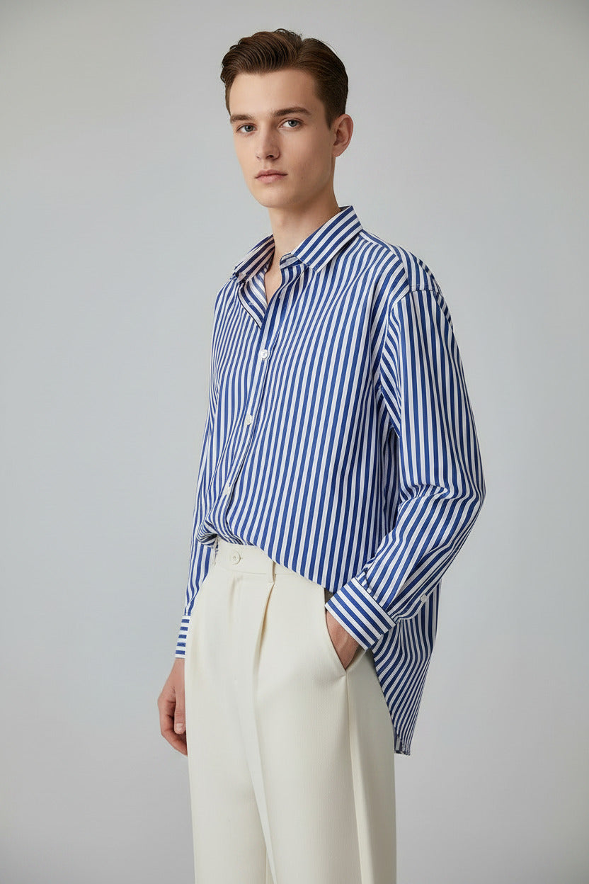 Blue and white striped shirt on a hanger with a white curtain and brown bag in the background.