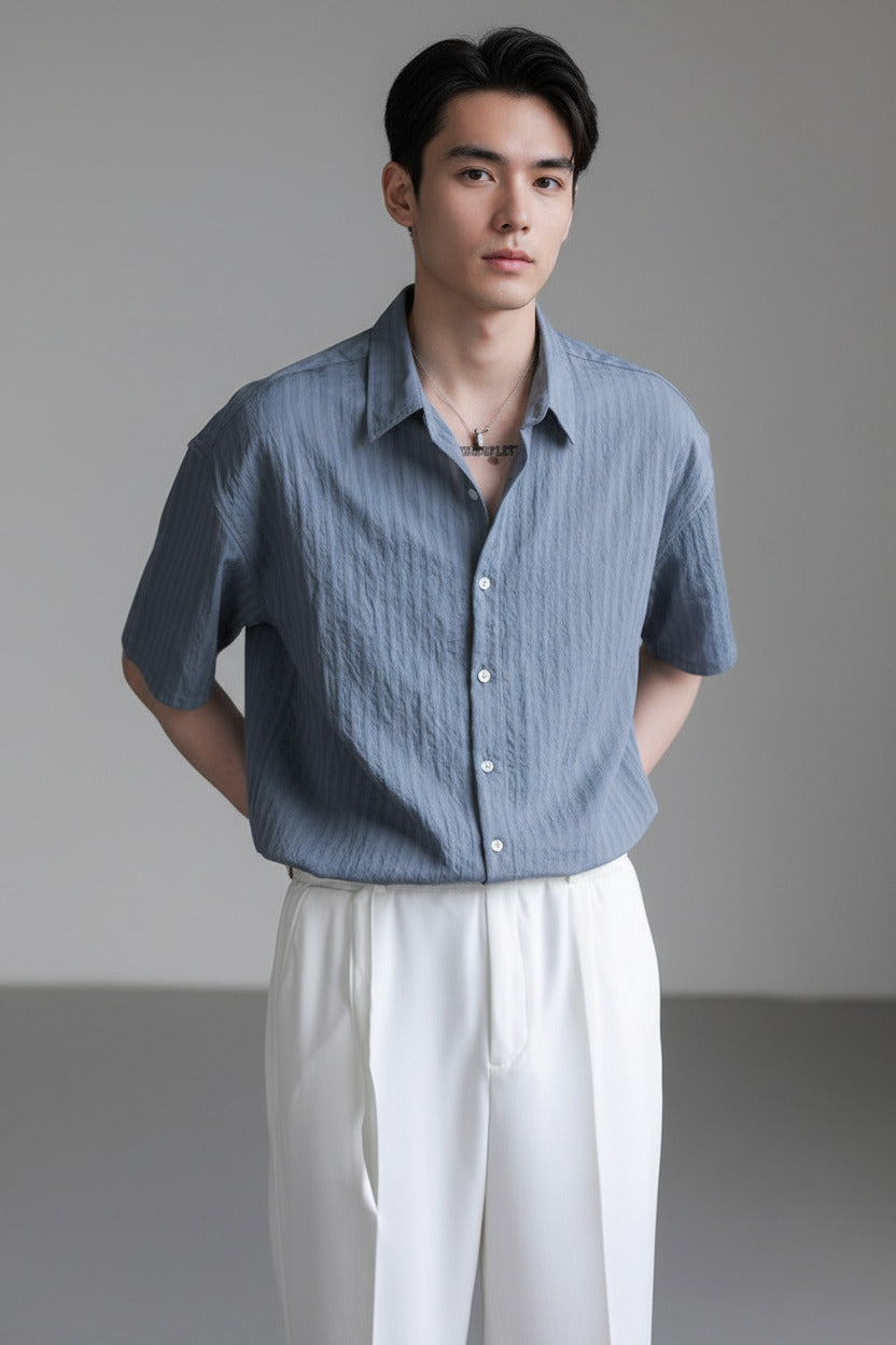 Person wearing a blue short-sleeve shirt and white pants against a gray background