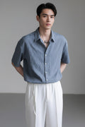 Person wearing a blue short-sleeve shirt and white pants against a gray background