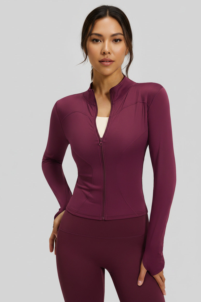A woman modeling a fitted long-sleeve athletic zip-up top in plum red, paired with matching leggings, against a light gray background. A small inset in the lower left shows the top alone with the text 'Plum red'.