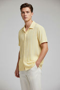 A man wearing a pale yellow short-sleeve button-up shirt with a textured vertical stripe pattern, paired with white pants.