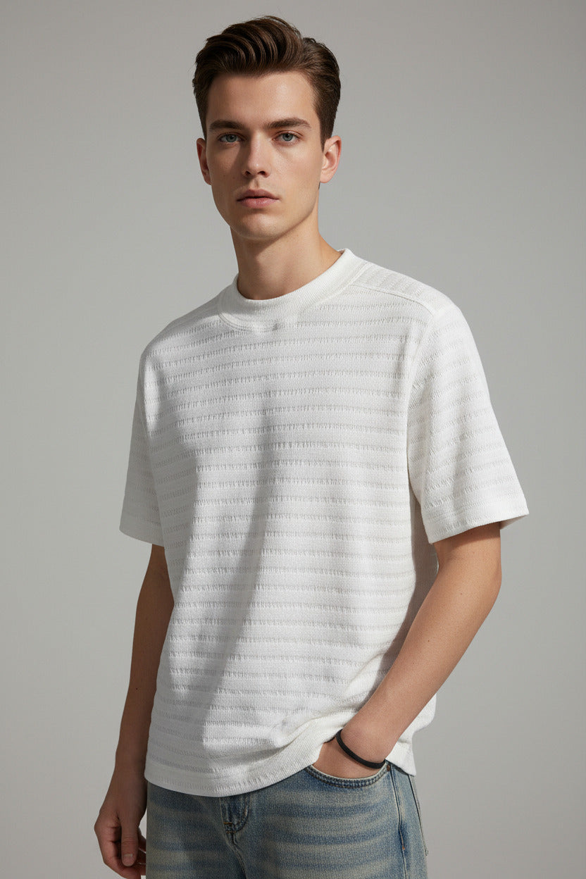 Person wearing a textured white t-shirt and light-colored pants against a dark background