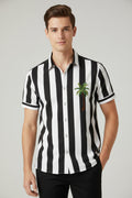 A men's short-sleeve button-up camp shirt with a black and white vertical stripe pattern, featuring a small green palm tree graphic on the left chest, displayed on a wooden hanger against a light gray background.