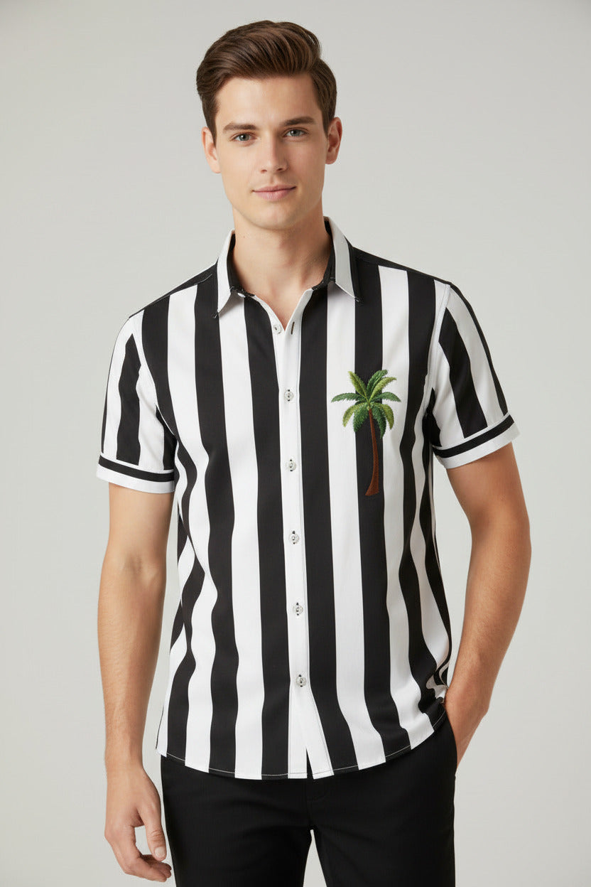 A men's short-sleeve button-up camp shirt with a black and white vertical stripe pattern, featuring a small green palm tree graphic on the left chest, displayed on a wooden hanger against a light gray background.