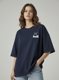 A dark navy blue short-sleeve t-shirt with a small cartoon cat graphic on the left chest, laid flat on a white faux fur surface.